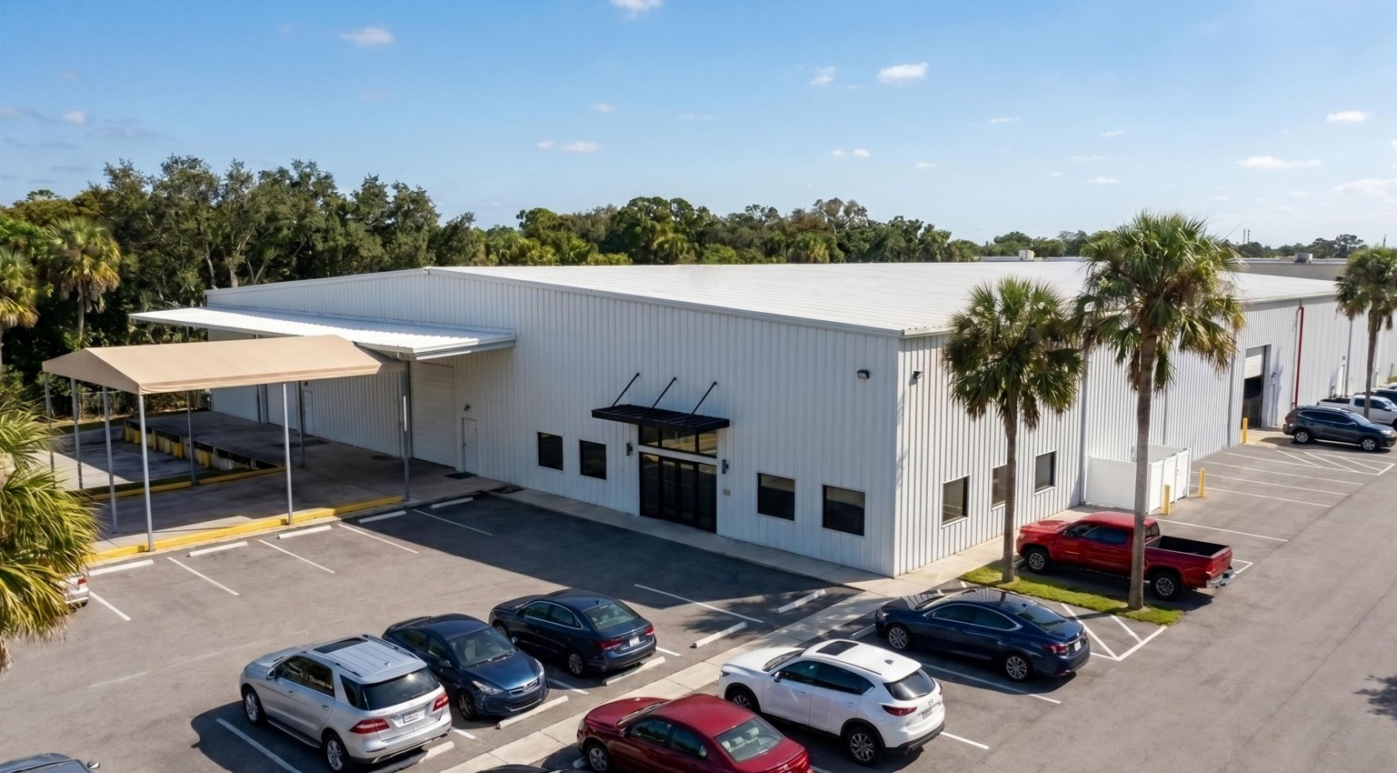 Aerial view of 198 Lock Road, a freestanding warehouse for lease in Deerfield Beach, Florida, with a covered loading/staging canopy, palms and a striped parking field.